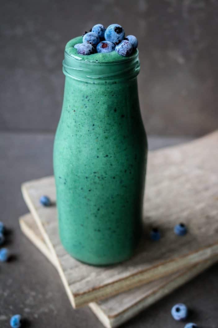 Glowing Green Spirulina Smoothie in a glass from the side with blueberries