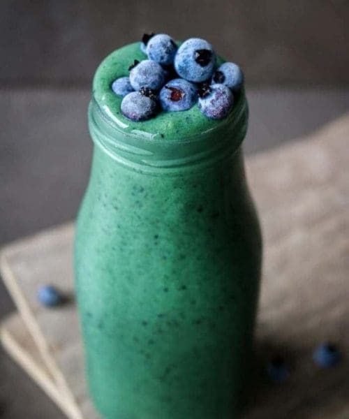 Glowing Green Spirulina Smoothie in a glass with blueberries on top
