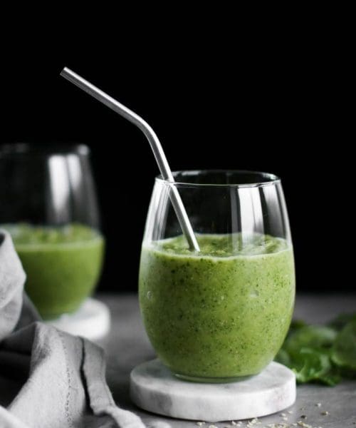 Two glasses of New Year Tropical Green Smoothie with a straw seen from the side