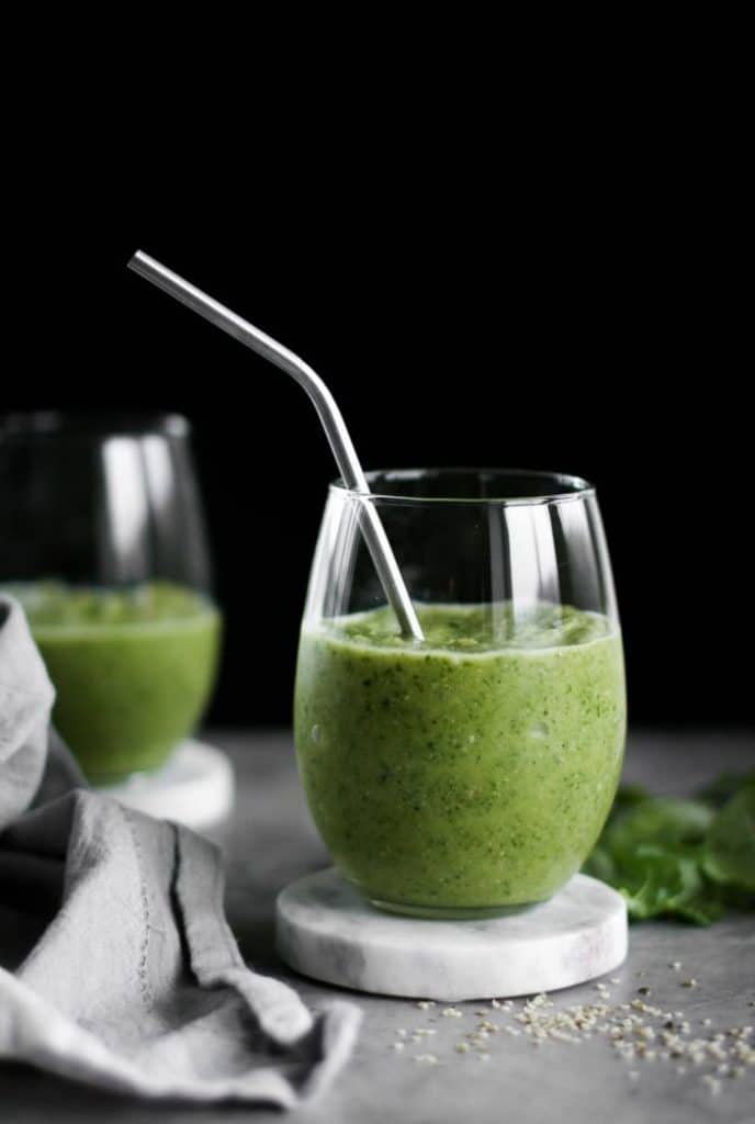 Two glasses of New Year Tropical Green Smoothie with a straw seen from the side 