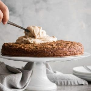 hand adding frosting to an apple zucchini cake