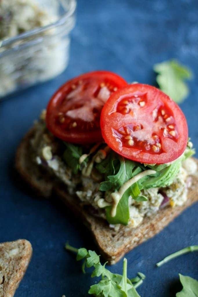 open face chickpea salad sandwich with greens and tomatoes