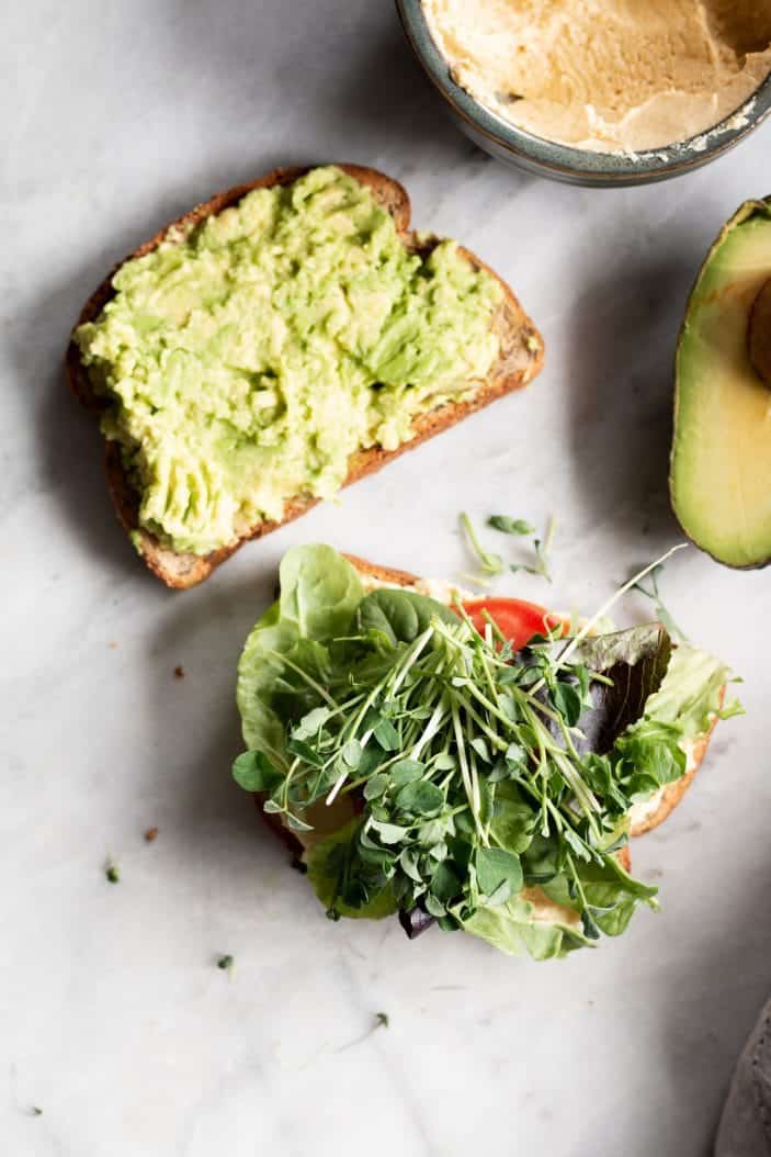open hummus and avocado sandwich with greens