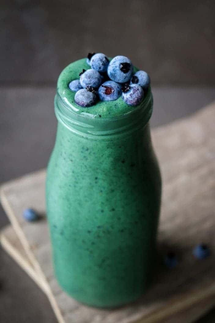 glowing green spirulina smoothie in a glass with blueberries on top