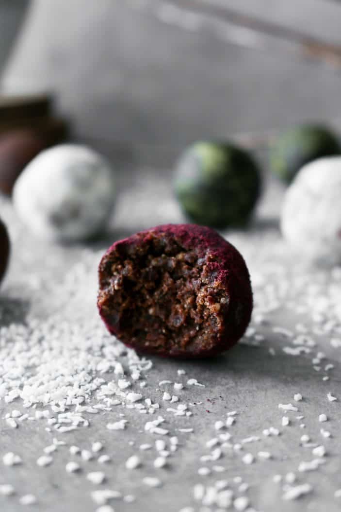 Six Easy Holiday Truffles seen from the side with one that has a bite taken from it, in different colours ranging from red, white and green.