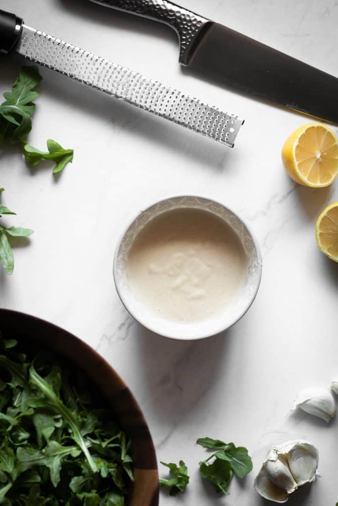 tahini dressing in a bowl with lemons and arugula