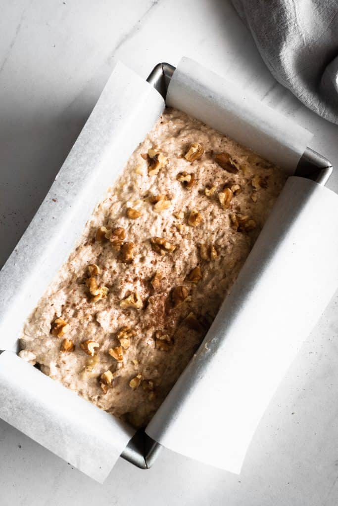 banana bread mixture in loaf pan with walnuts