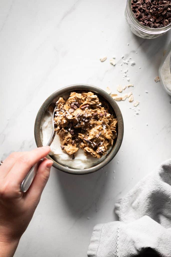 hand holding spoon in granola bowl