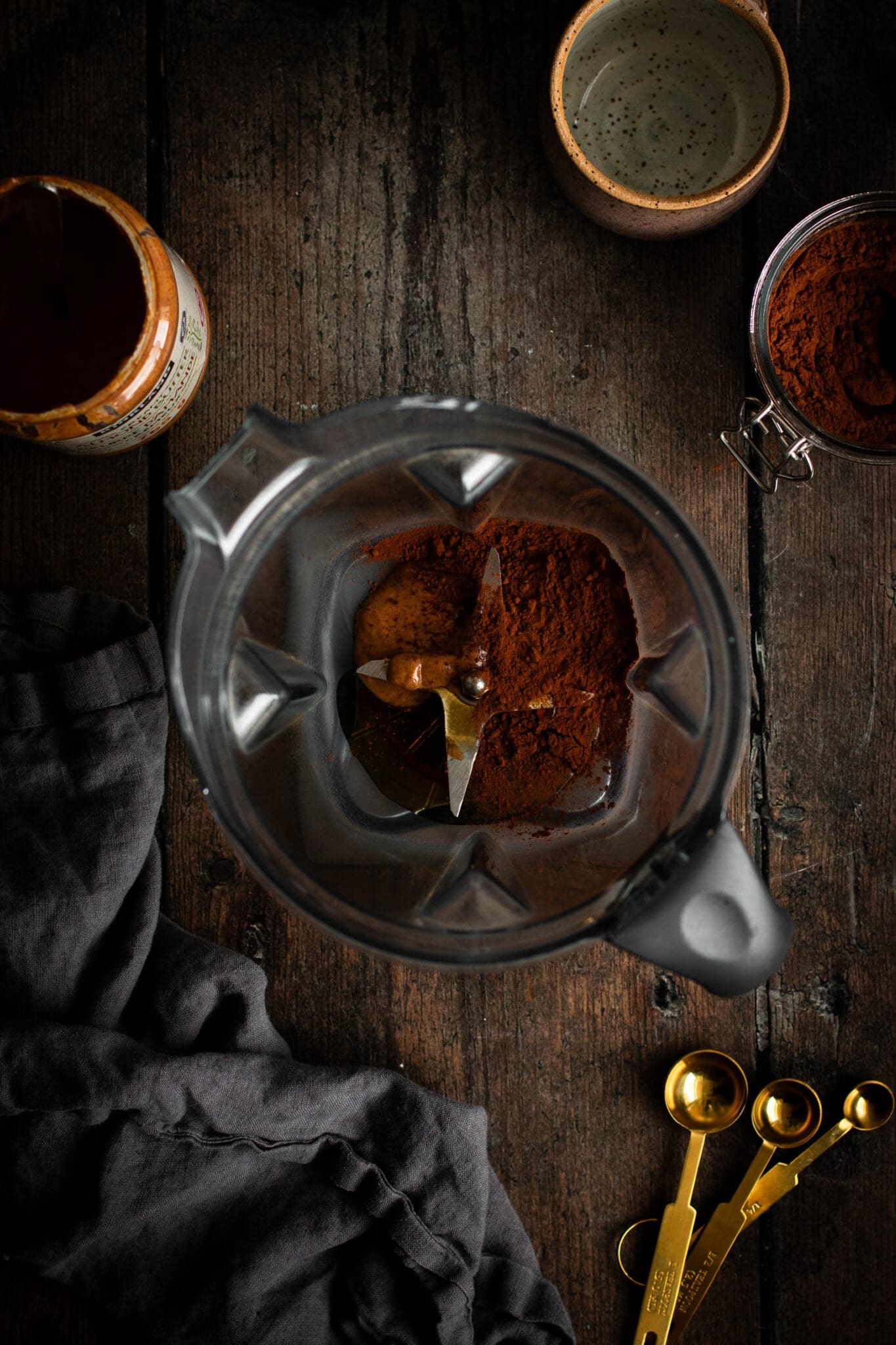 Cocoa powder, maple syrup and almond butter in a blender, seen from the top.