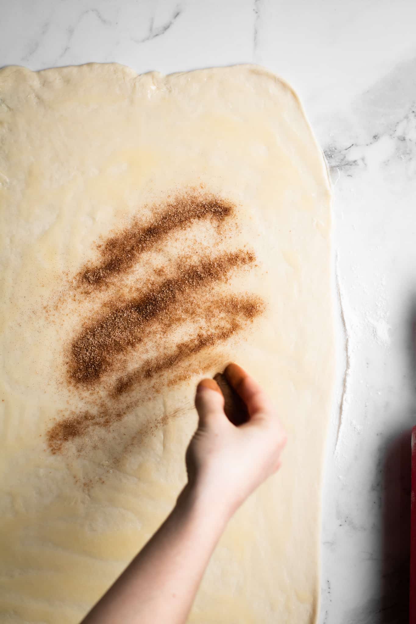 Hand dusting cinnamon sugar over the dough