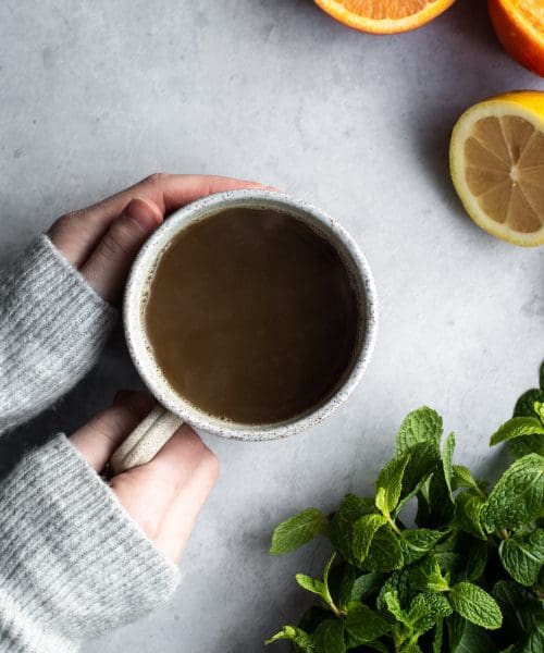 hand holding a cup of tea with citrus and mint