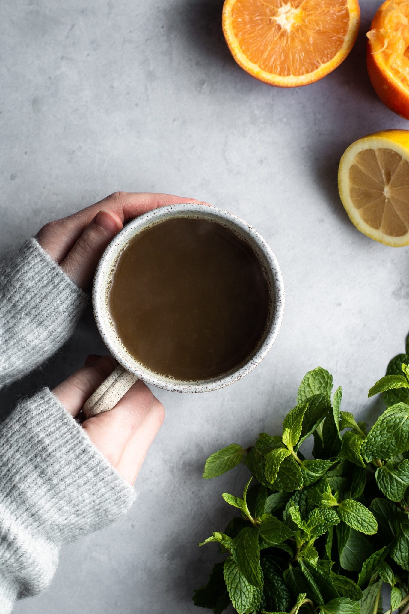 hand holding a cup of tea with citrus and mint