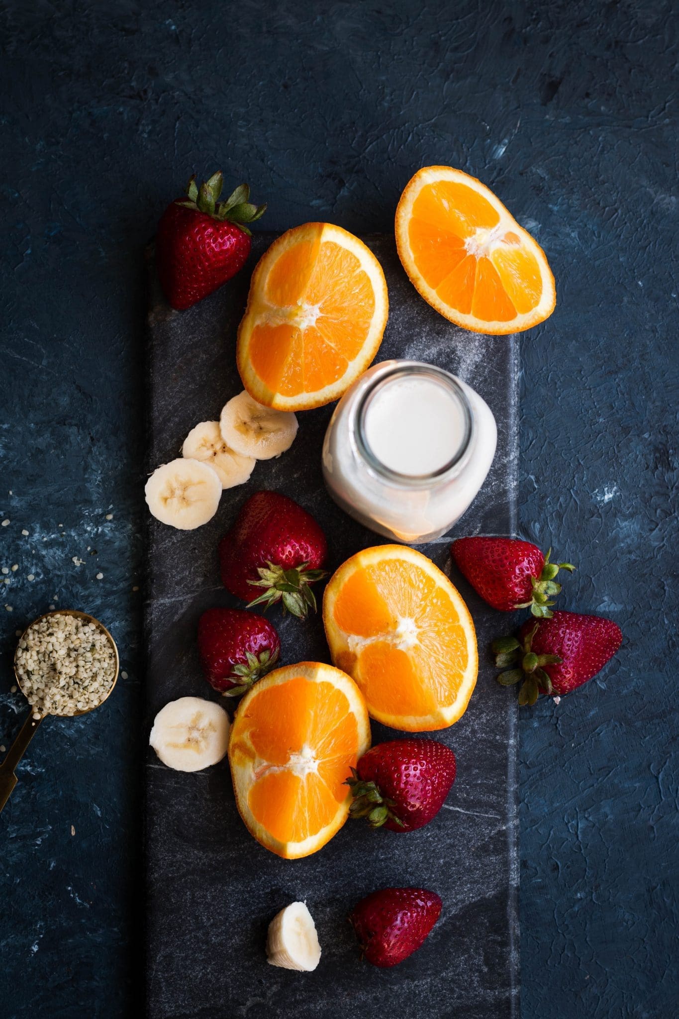 Oranges, bananas, strawberries and a glass of milk seen from the top.