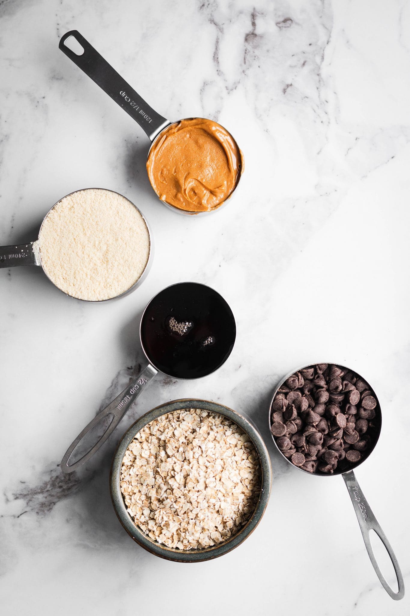 peanut butter, almond flour, maple, oats and chocolate in measuring cups