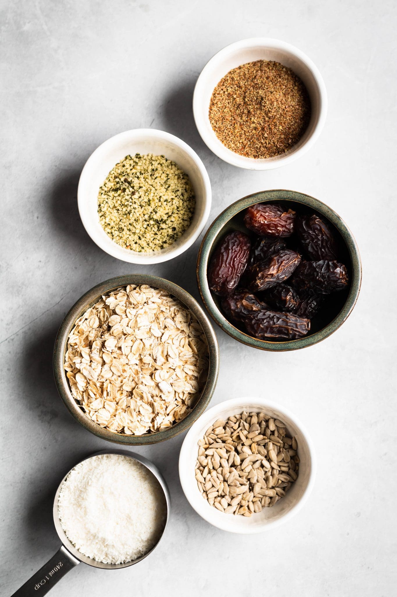 oats, dates, coconut, sunflower seeds, hemp hearts and flax seeds in bowls.