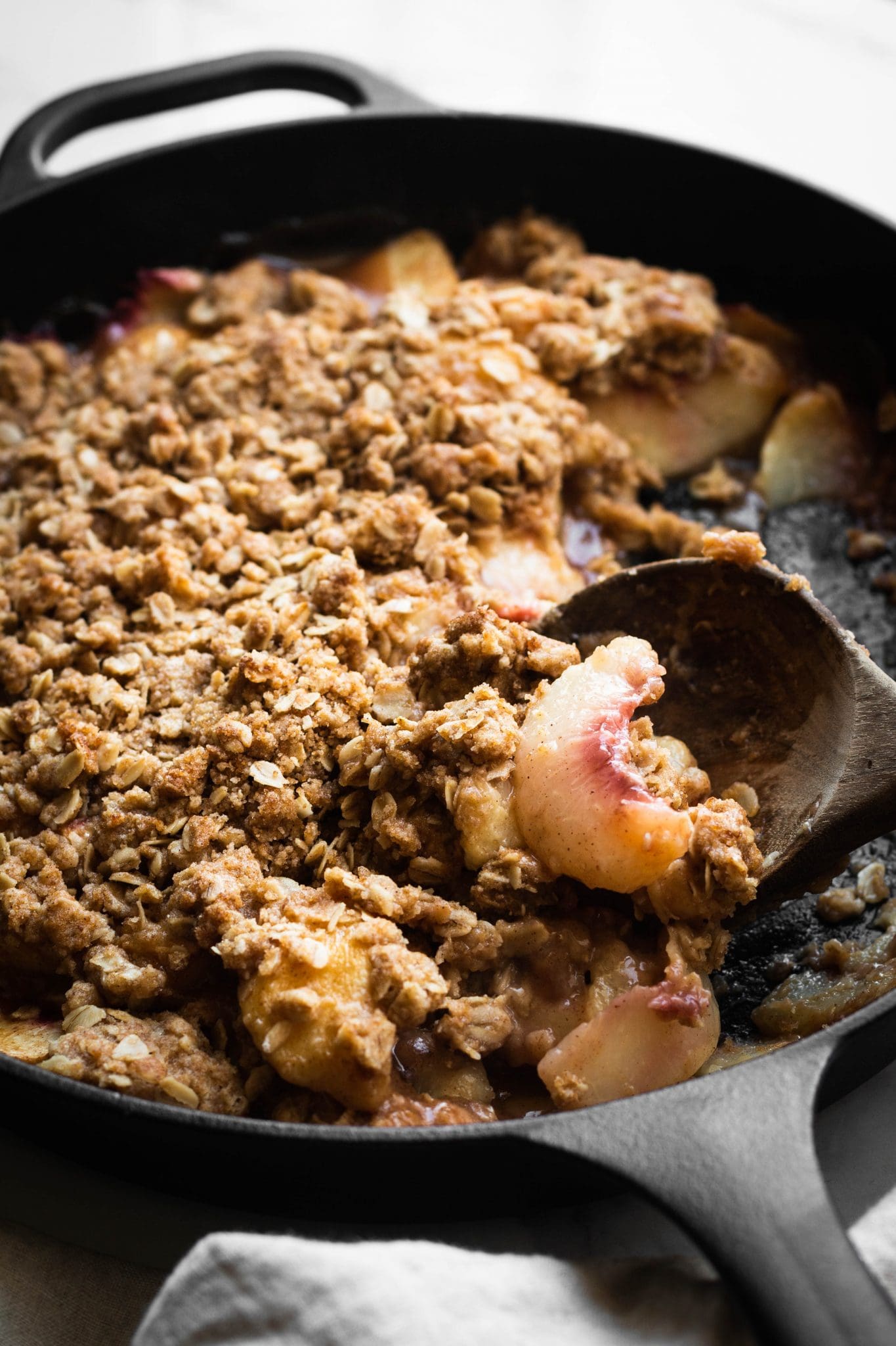 closeup of peach crisp in a cast-iron skillet with a serving spoon