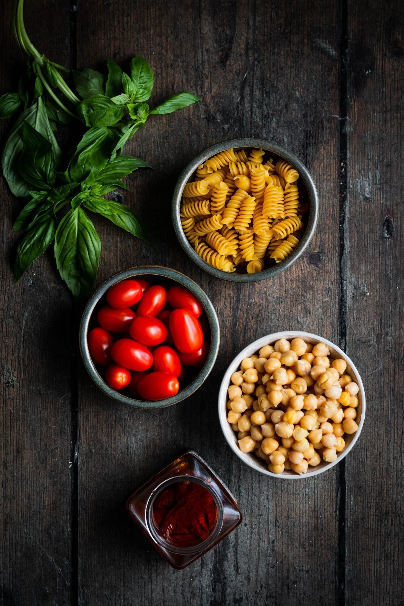 pasta, cherry tomatoes, chickpeas, sundried tomatoes in bowls, plus basil leaves