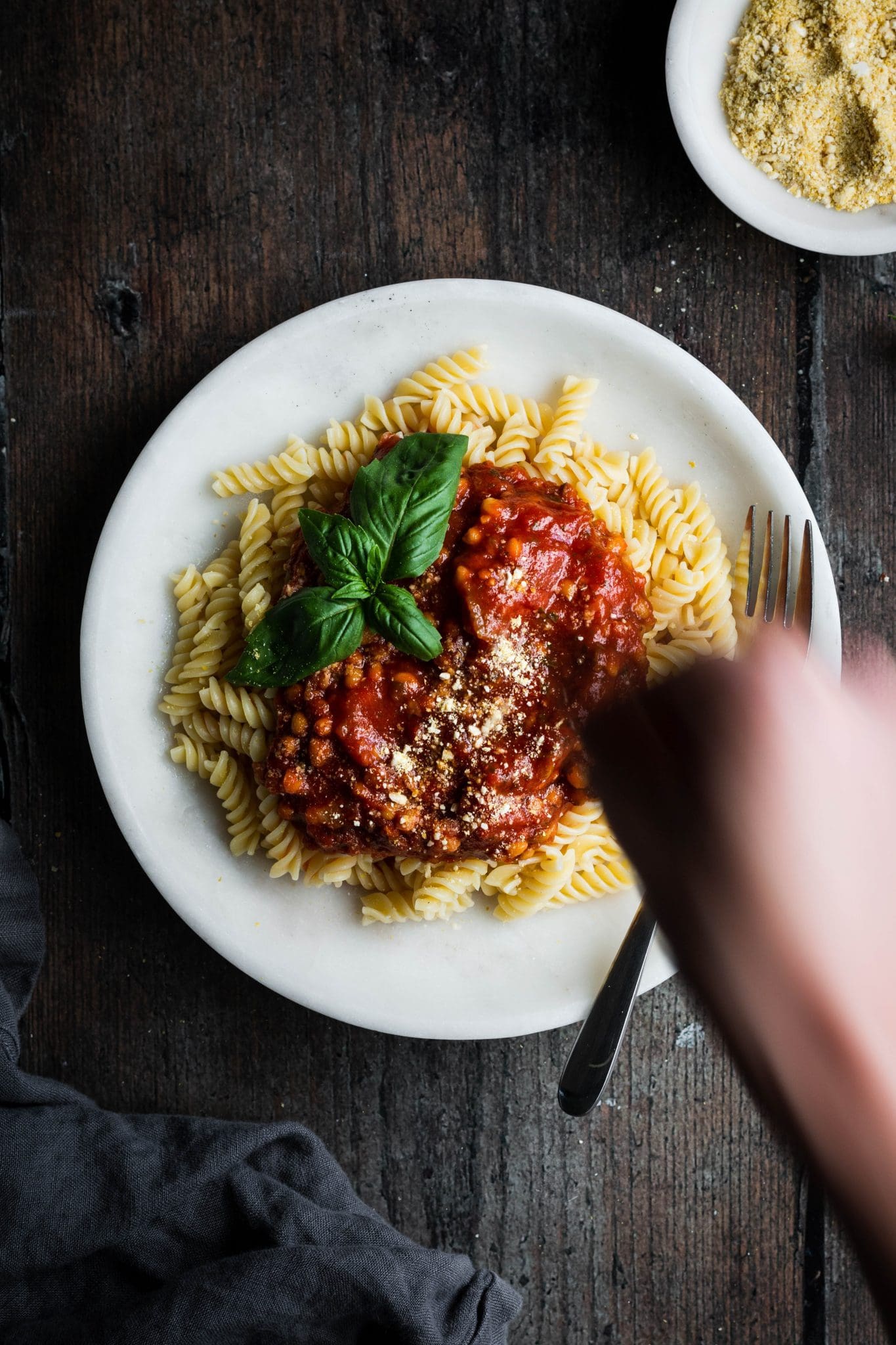 hand sprinkling vegan parmesan on lentil tomato pasta