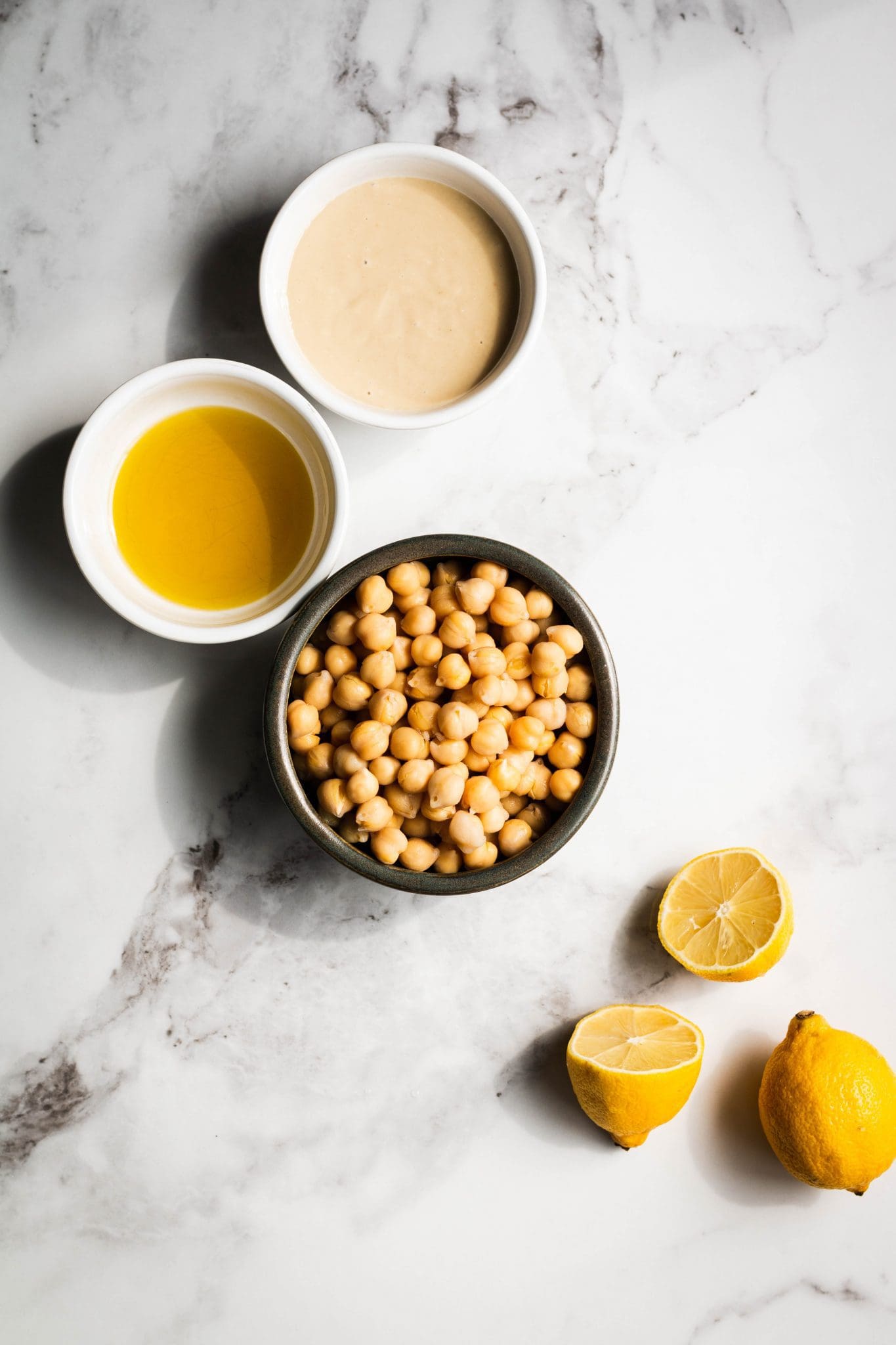 chickpeas, tahini and oil in small bowls, plus lemons on the side