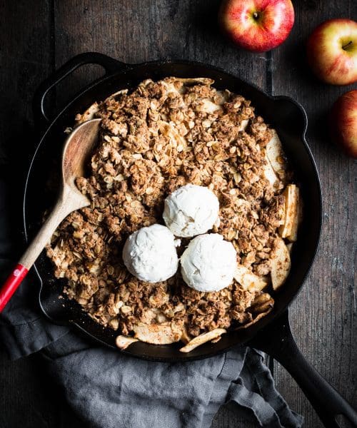 apple crisp in a cast-iron skillet with 3 scoops of ice cream on top