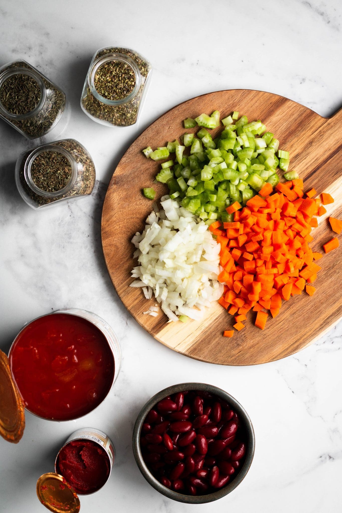 diced carrots, onions and celery on a cutting board with herbs, beans and canned tomatoes on the side