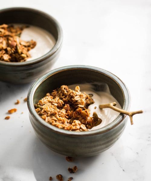 two bowls of yogurt with maple flax pumpkin seed granola