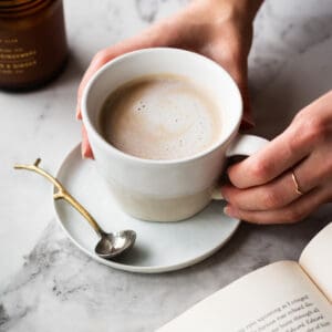 Hands holding a cup of London Fog tea latte with a book and candle on the side