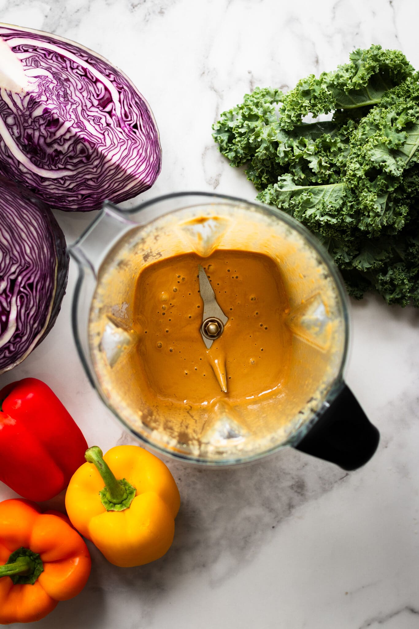 The best nutritional yeast dressing in a blender, seen from the top with cabbage, kale and bell peppers on the side