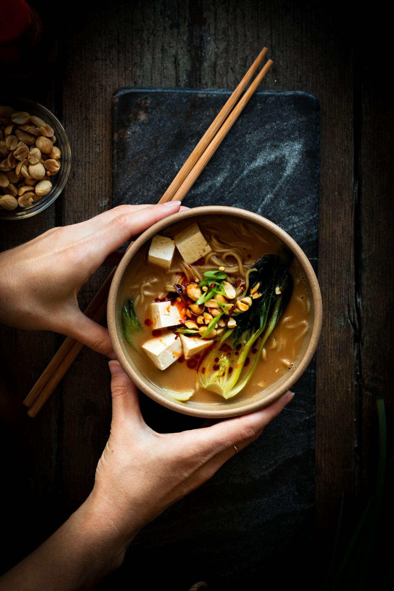 hands holding a bowl of vegan ramen with tofu and Bok choy