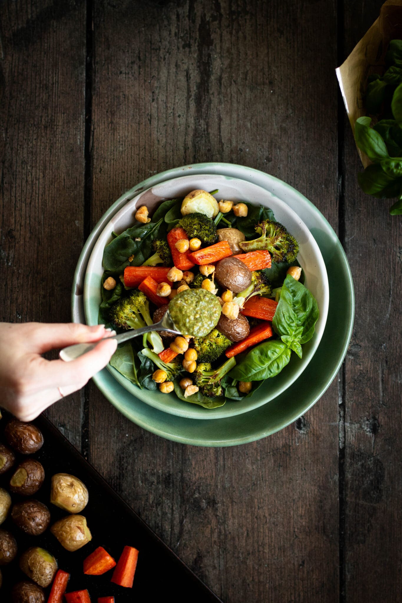 spoonful of pesto added to a bowl of roasted vegetables seen from the top