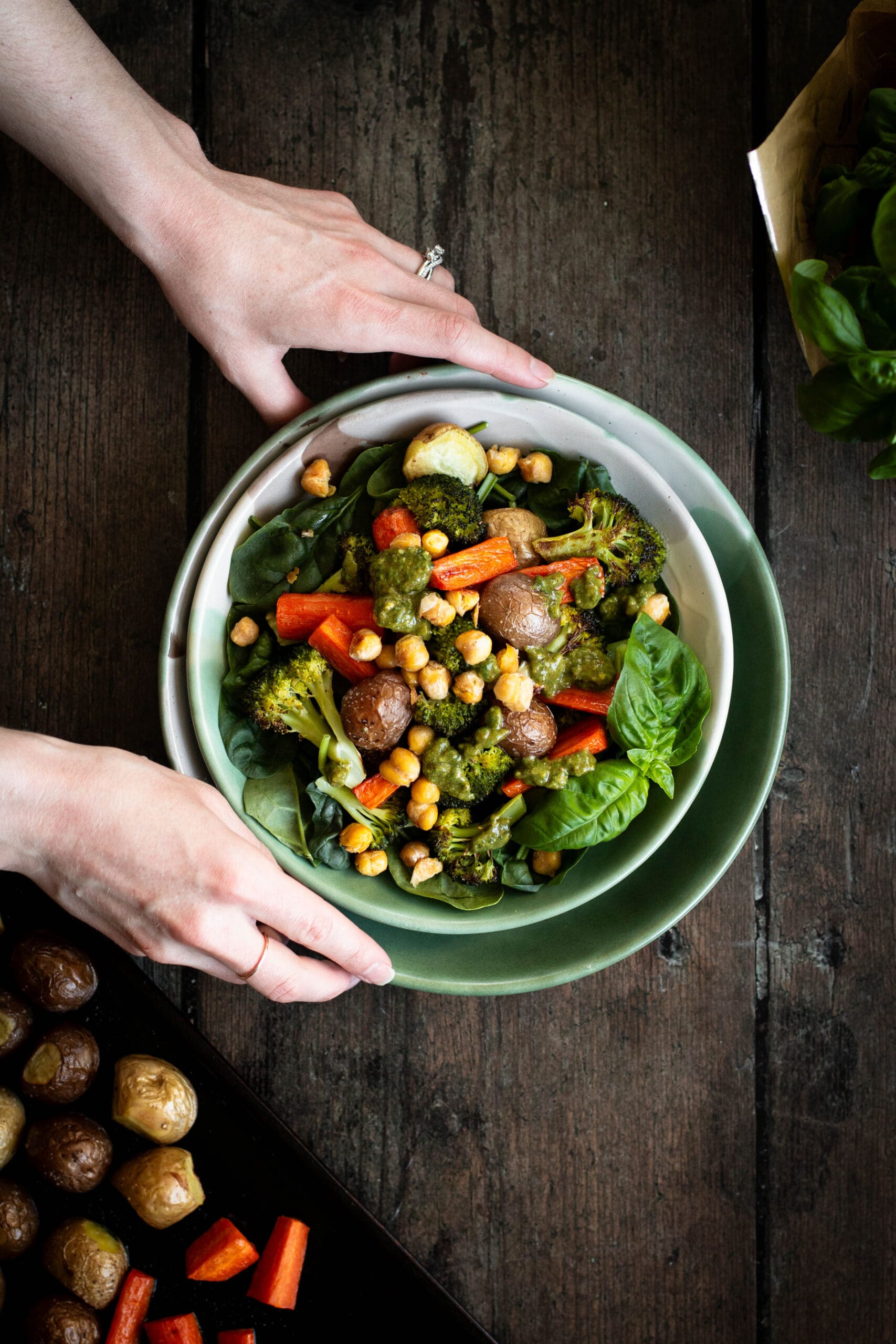 hands holding a bowl of roasted vegetables with almond pesto seen from the top