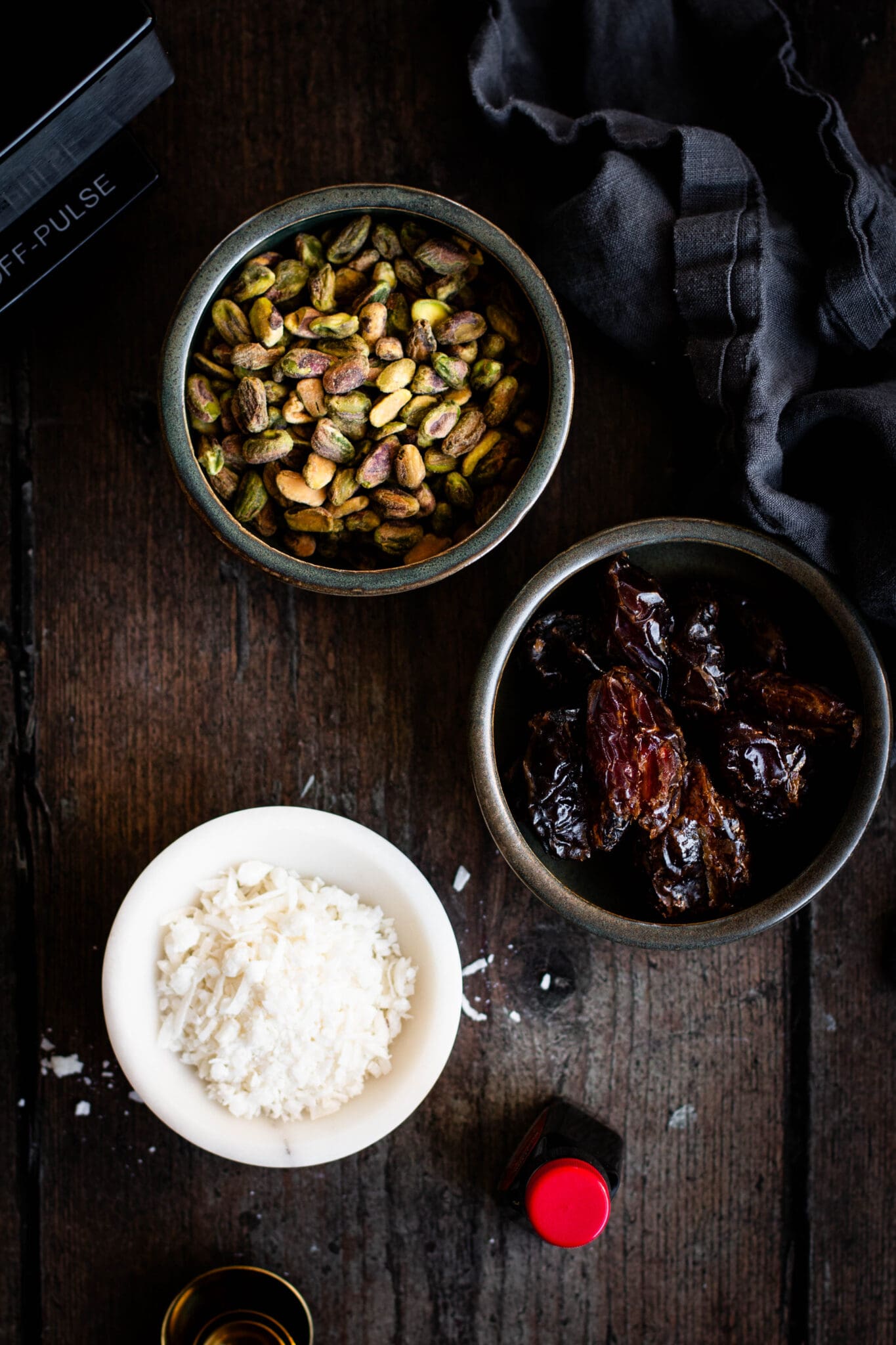Pistachios, dates and coconut in bowls seen from the top.