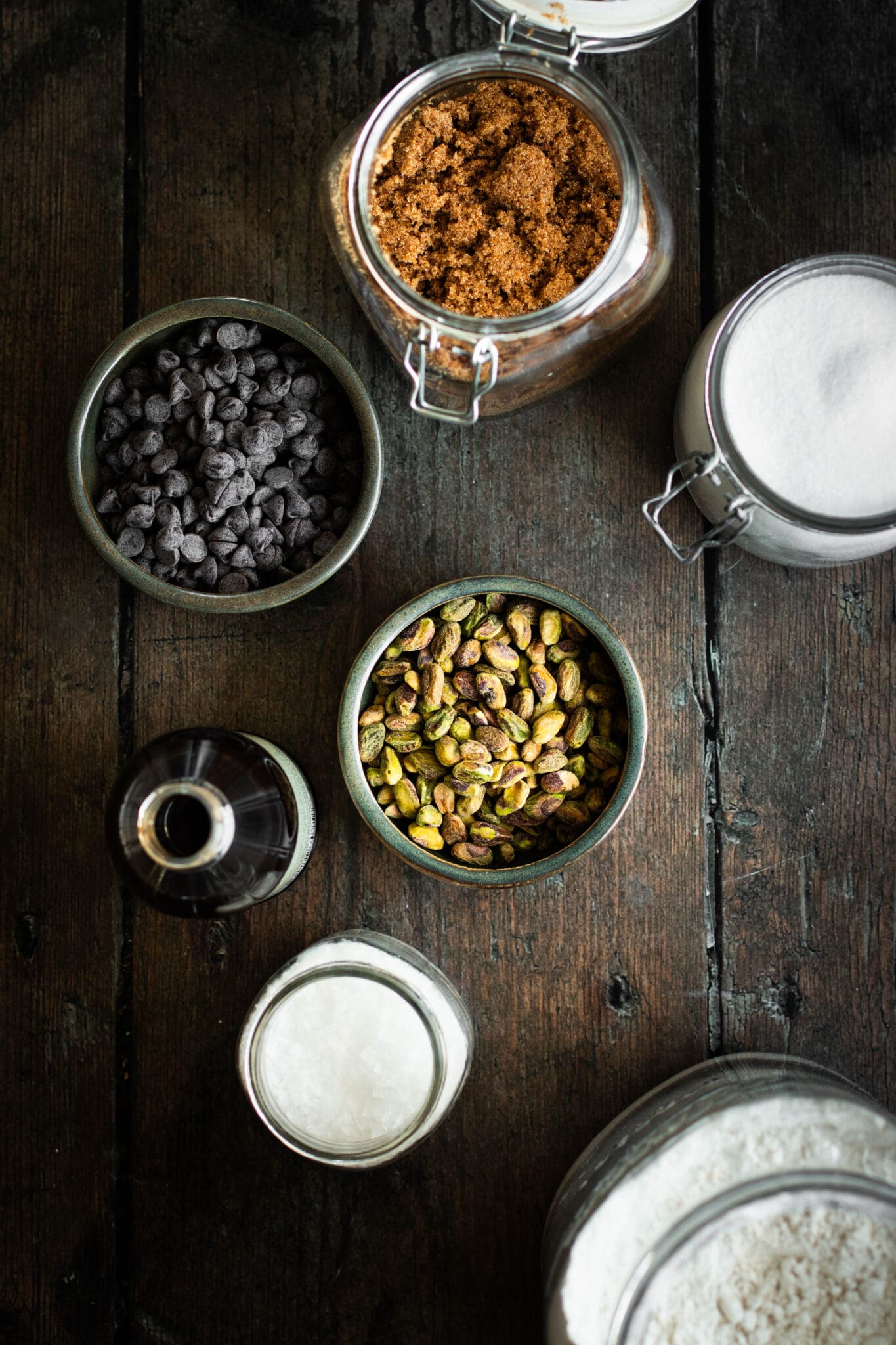 Brown sugar, granulated sugar, chocolate chips, pistachios, vanilla extract, salt and flour seen from the top.