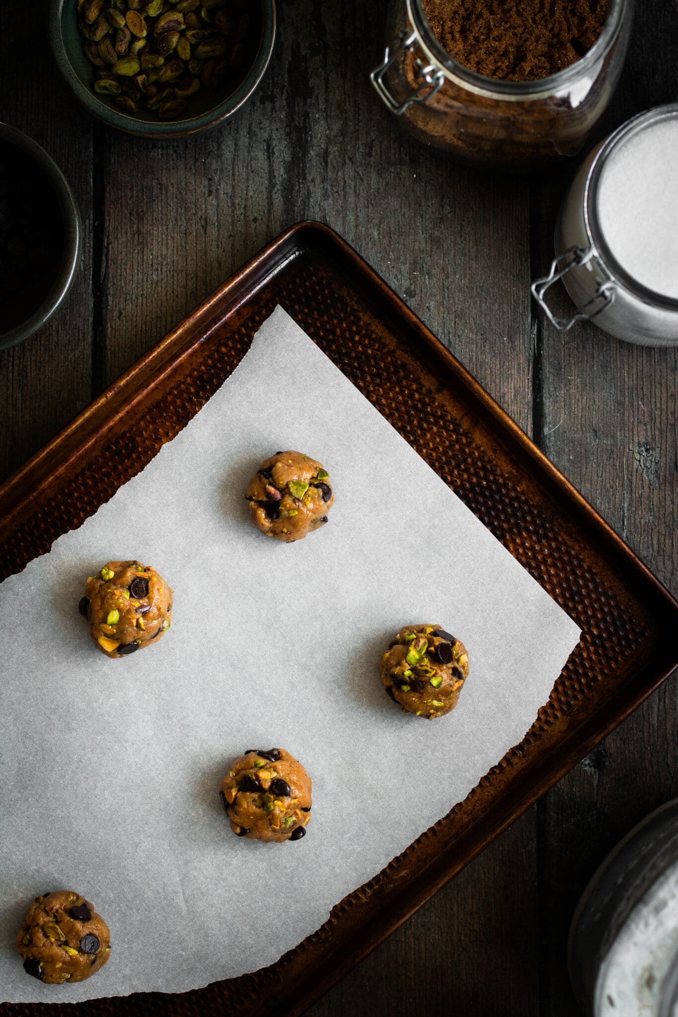 Salted pistachio chocolate chip cookie balls on a baking sheet.
