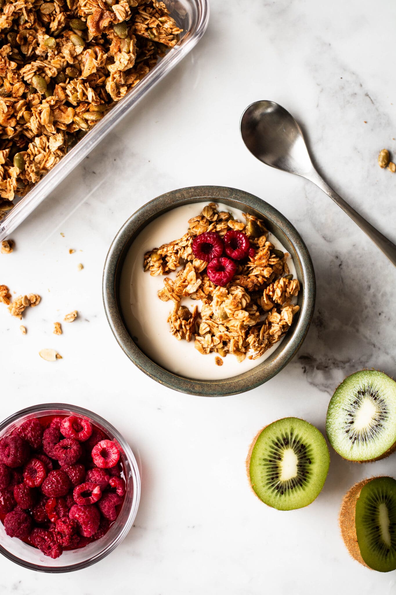 granola in a bowl with yogurt, raspberries, and kiwi on the side
