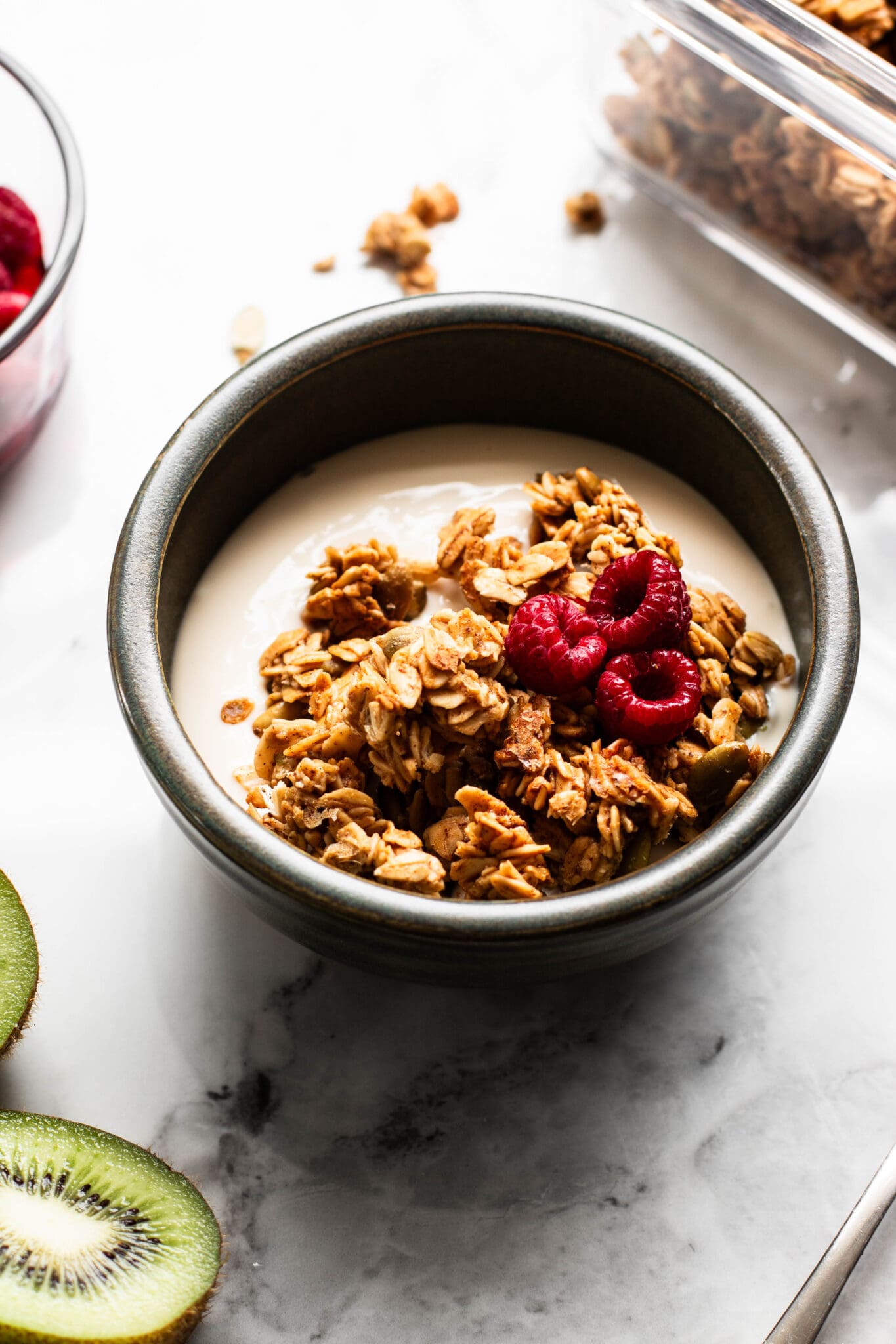 Weekly meal prep granola in a bowl with yogurt and raspberries, and kiwi on the side