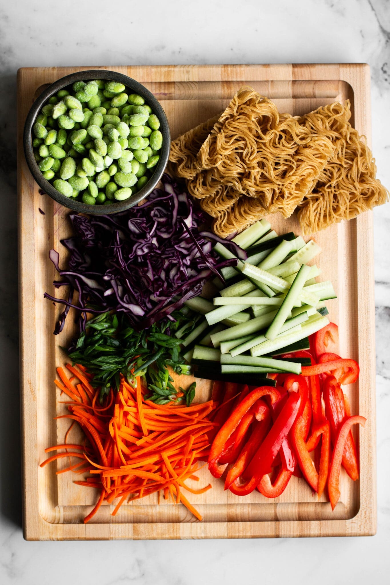 Chopped vegetables, edamame and ramen noodles on a cutting board.
