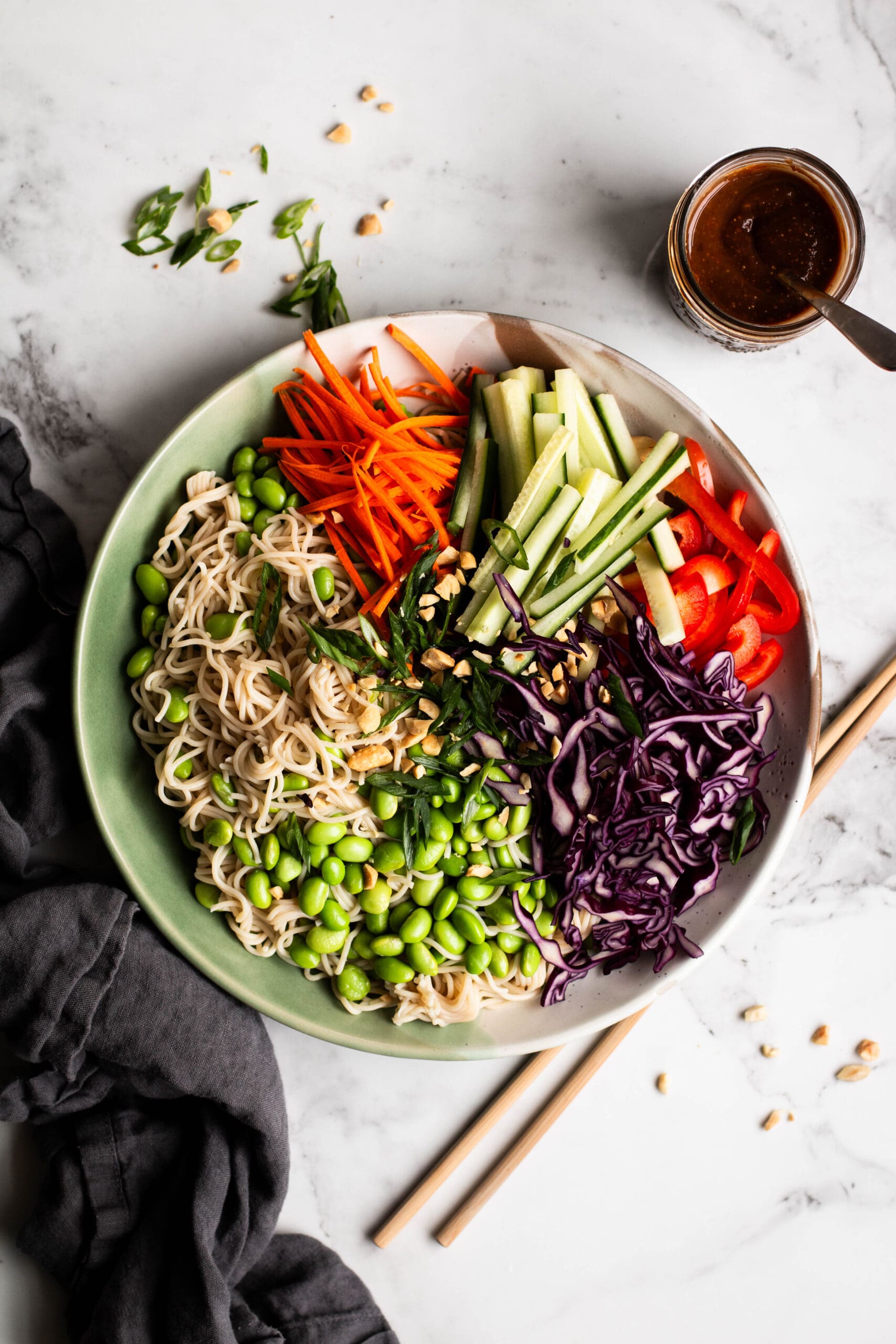Peanut noodle salad with edamame and vegetables in a large bowl with peanut sauce on the side.